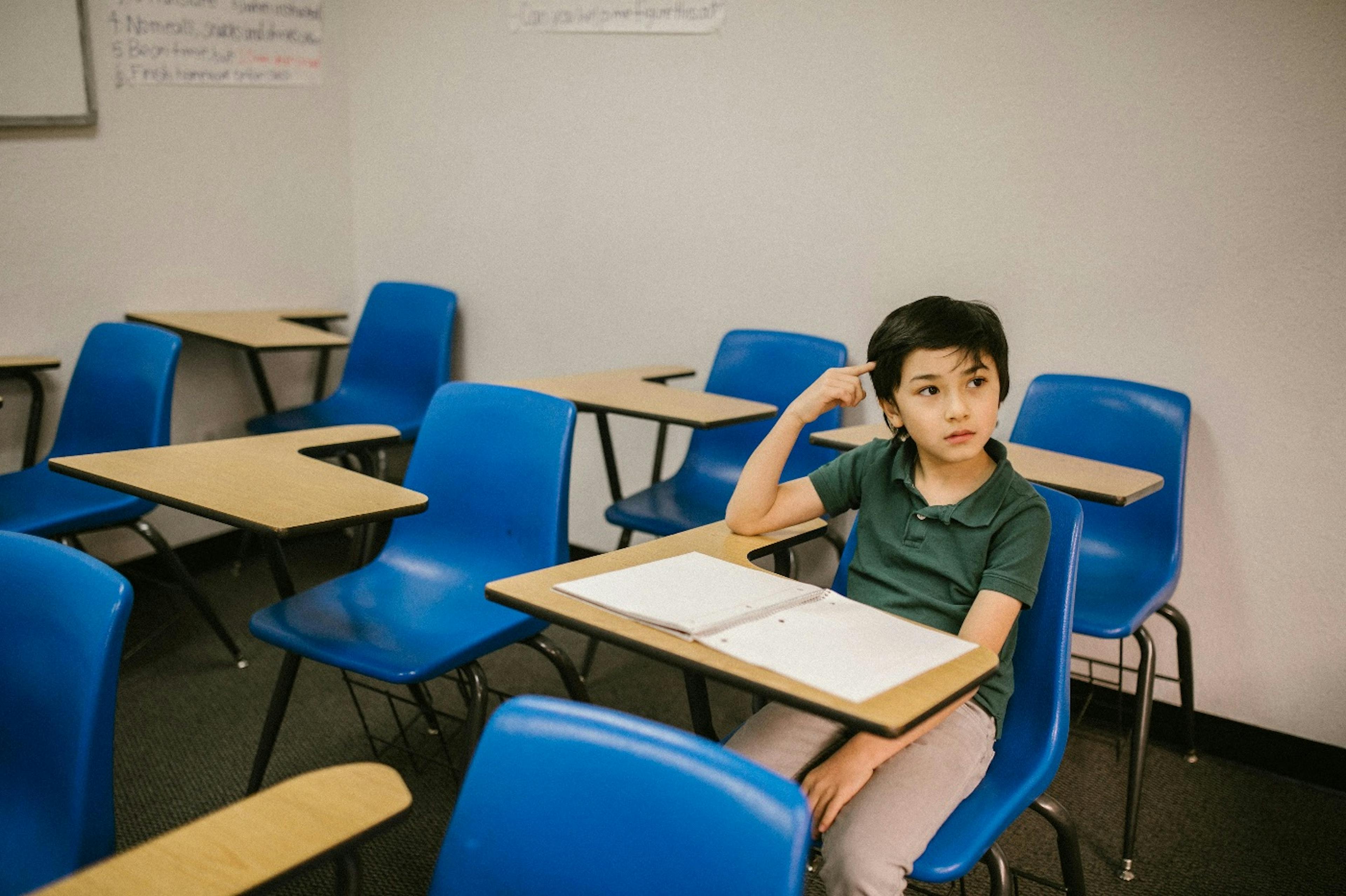 The kid is sitting in the classroom thinking.