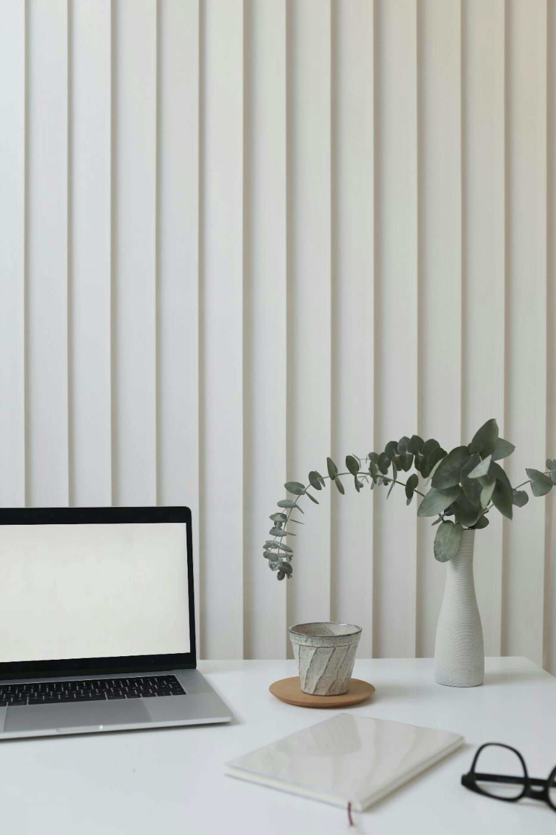 Ein Schreibtisch mit Laptop, Tasse, Blume, Notizbuch und Brille.