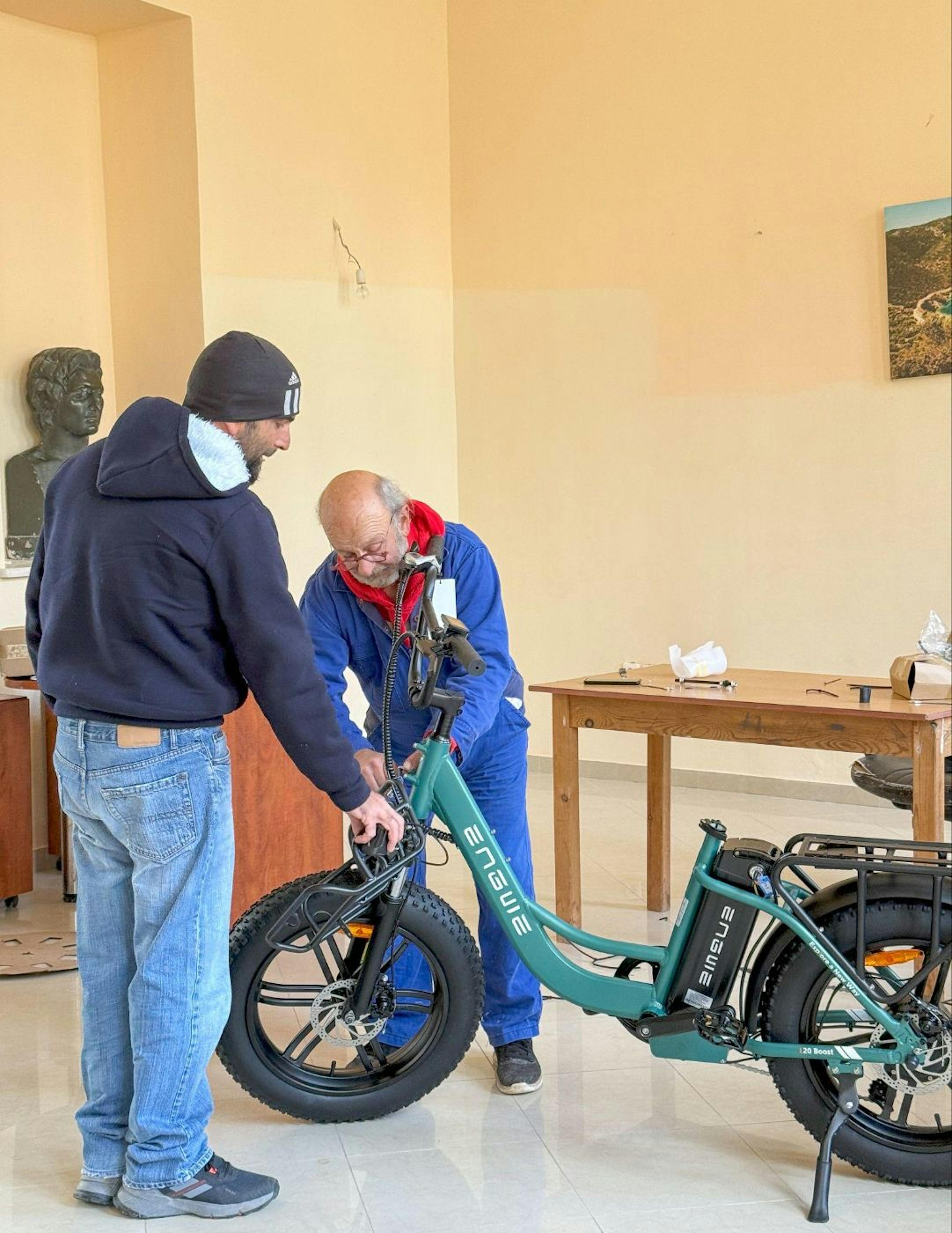 Akis and Spiros (Papis), two local residents, are working together assembling the e-bikes in one of Kalamos' communal spaces.